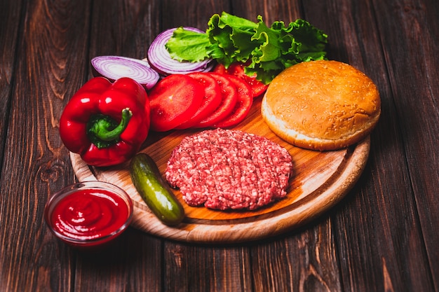 Carne de res molida cruda Chuletas de filete de hamburguesa con condimento, queso, tomate, ensalada y pan sobre tablas de madera vintage