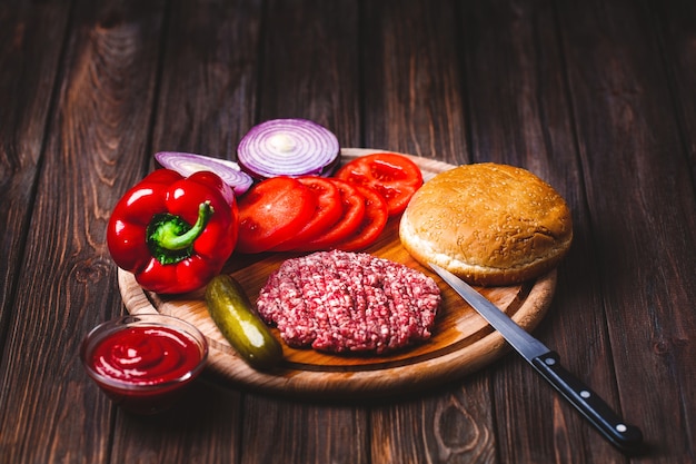 Carne de res molida cruda Chuletas de filete de hamburguesa con condimento, queso, tomate, ensalada y pan sobre tablas de madera vintage