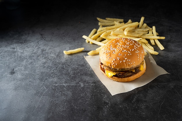 Carne de res o cerdo. Hamburguesa y papas fritas sobre fondo oscuro