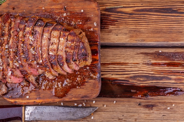 Carne de res a la parrilla en rodajas Filete de ternera con especias en tabla de cortar de madera rústica