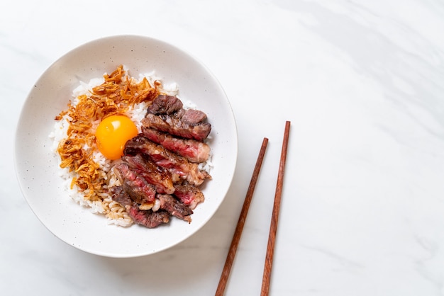 carne en rodajas en un tazón de arroz cubierto con huevo