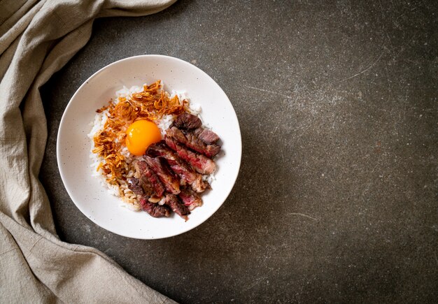 carne en rodajas en un tazón de arroz cubierto con huevo