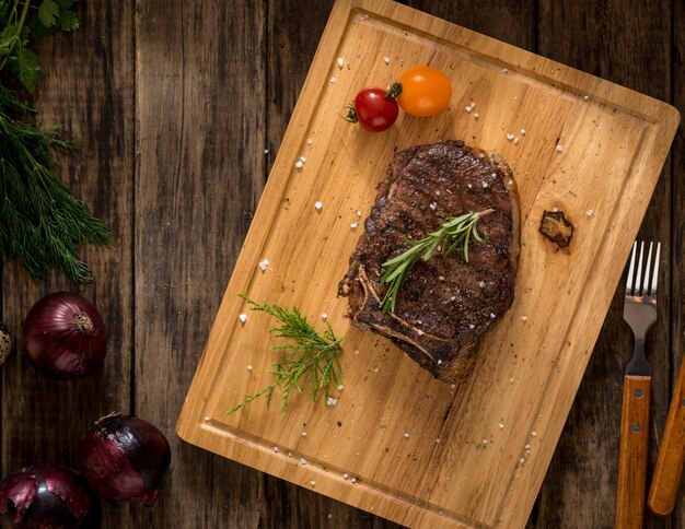 Carne suculenta adornada com tomate e cebola em fundo de madeira, vista superior