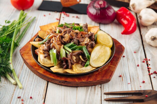 Carne de ternera frita con patatas en la mesa de madera