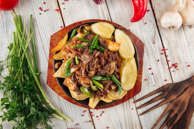 Carne de ternera frita con patatas en la mesa de madera