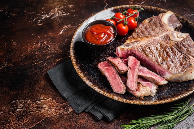 Carne de ternera porterhouse a la parrilla Bistec cocido en un plato con tomate Fondo oscuro Vista superior Espacio de copia