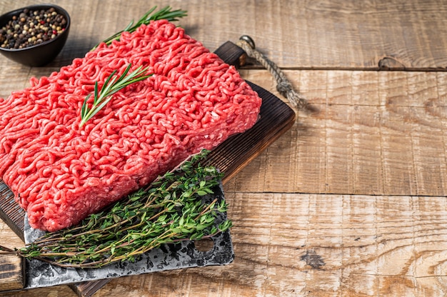 Carne de vacuno picada fresca cruda en una tabla de cortar de carnicero con cuchilla. Fondo de madera. Vista superior. Copie el espacio.