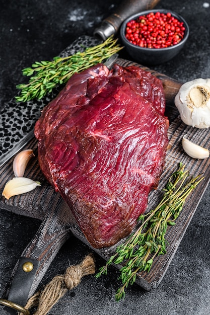 Carne de venado cruda de venado en una tabla de corte con hierbas. Vista superior.