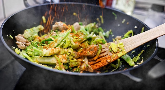 La carne con verduras frescas cocinadas en una sartén wok asiática se espolvorea pimienta roja molida seca sobre la comida