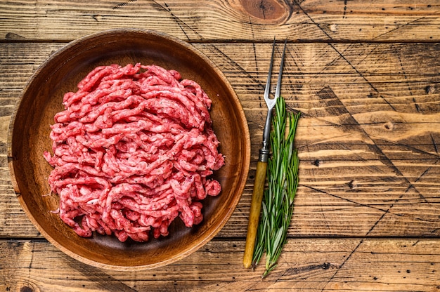 Carneiro cru, carne de carneiro moída com ervas em um prato. fundo de madeira. vista do topo. copie o espaço.