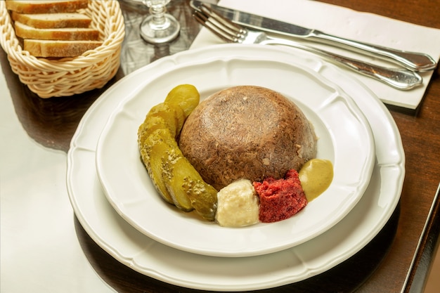 Carnes gelatinosas caseiras, com pepino em lata cortado, temperos, mostarda e pão servidos em restaurante. Comida festiva do norte tradicional.