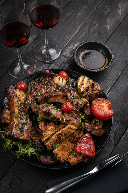 Carnes grelhadas variadas com molho e vinho tinto em mesa preta