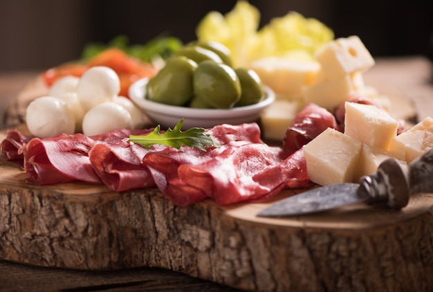 Foto carnes variadas e um prato de queijo, em uma tábua de madeira. antepastos italianos