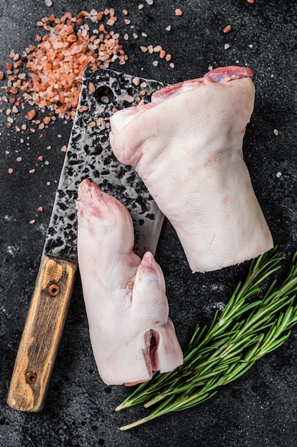 Foto carnicería - pezuña de cerdo cruda, nudillo, pies en una tabla de cortar. fondo negro. vista superior.