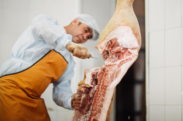 Carnicero cortando carne de cerdo en la industria cárnica