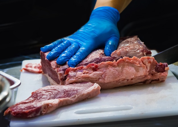 Carnicero cortando carne cruda con cuchillo en la cocina