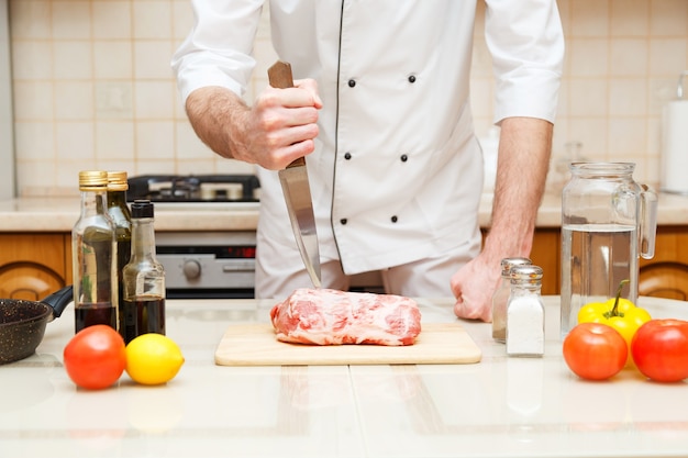 Carnicero cortando carne en tabla de cortar cocinero profesional sosteniendo un cuchillo y cortando carne