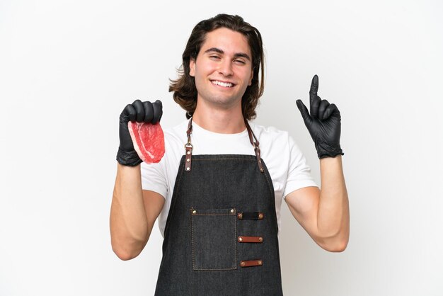 Un carnicero guapo con un delantal y sirviendo carne fresca cortada aislada de fondo blanco señalando una gran idea