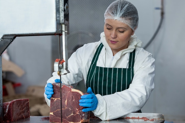 Carnicero hembra cortando carne cruda en una sierra de cinta