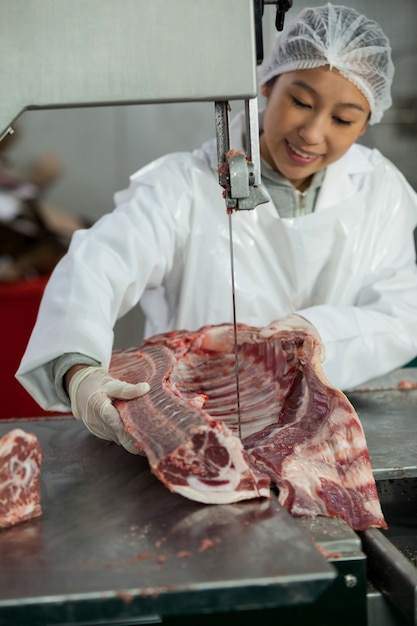 Carnicero hembra cortando carne cruda en una sierra de cinta