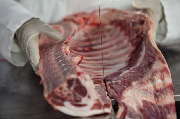 Carnicero hembra cortando carne cruda en una sierra de cinta