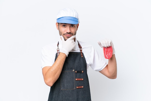 Carnicero hombre caucásico con un delantal y sirviendo carne fresca cortada sobre un fondo blanco aislado pensando