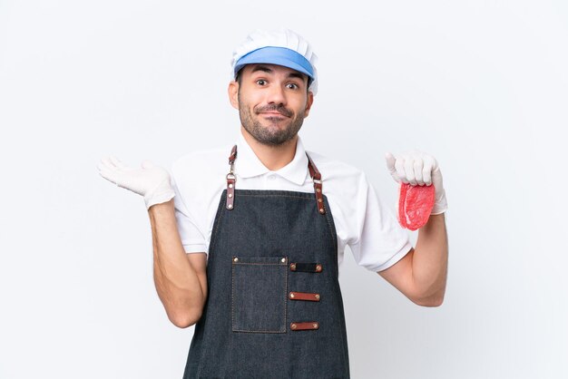 Carnicero hombre caucásico con un delantal y sirviendo carne fresca cortada sobre un fondo blanco aislado que tiene dudas mientras levanta las manos