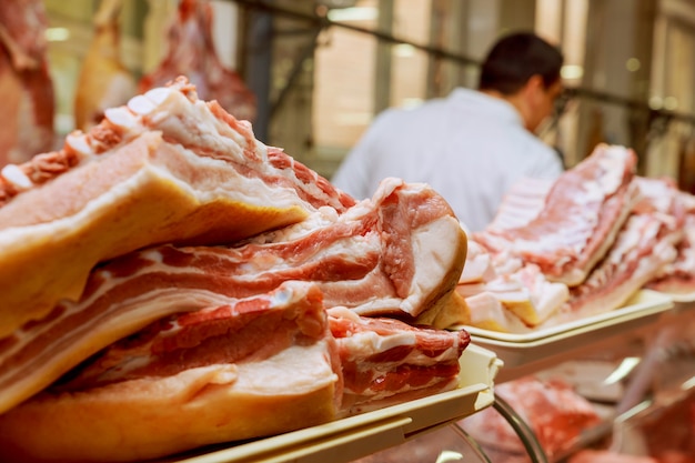 Carnicero masculino cortando carne cruda con cuchillo en mostrador en tienda