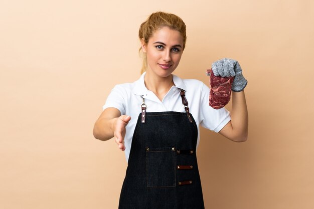 Carnicero mujer vistiendo un delantal y sirviendo carne fresca cortada sobre apretón de manos aislado después de un buen trato