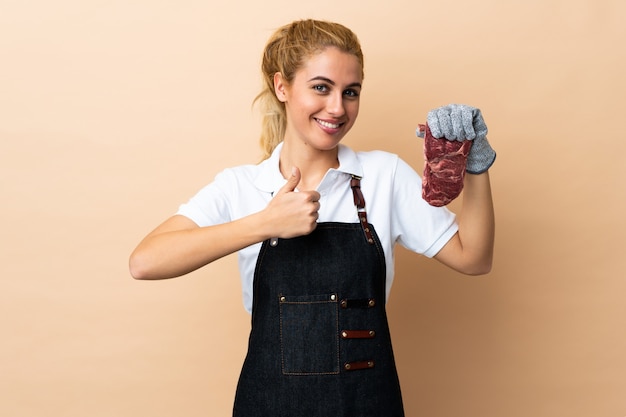 Carnicero mujer vistiendo un delantal y sirviendo carne fresca cortada sobre espacio aislado dando un gesto de aprobación