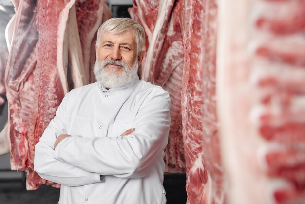 Carnicero de pie cerca de canales de cerdo con las manos cruzadas.