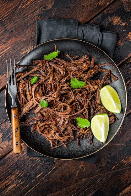 Carnitas en un plato con apio y rodajas de limón Fondo de madera Vista superior