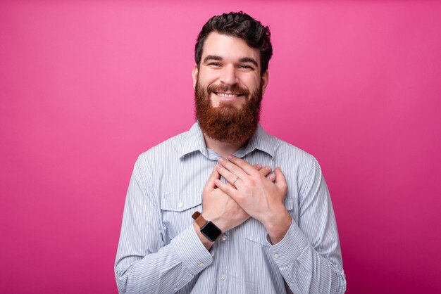 Caro meu coração. Homem barbudo mantém as mãos no coração, linda para a câmera no fundo rosa.