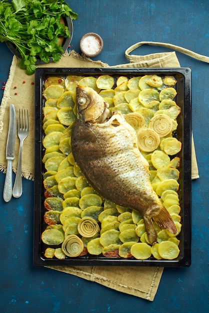 Carpa assada, peixe inteiro do forno com batatas fatiadas em uma bandeja grande