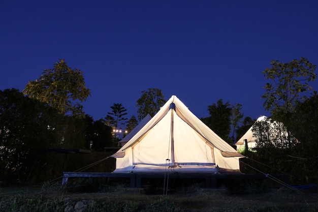 La carpa blanca está acampando en el jardín por la noche.