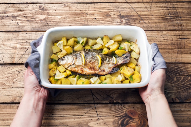 Carpa cozida dos peixes com batatas em uma bandeja cerâmica. Estilo rústico.