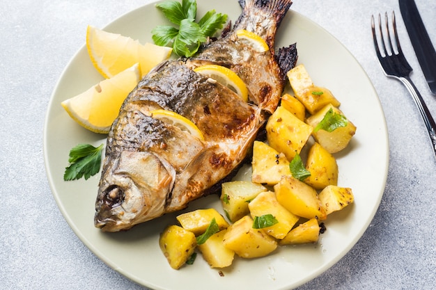 Carpa cozida dos peixes com verdes e batatas do limão em uma placa.