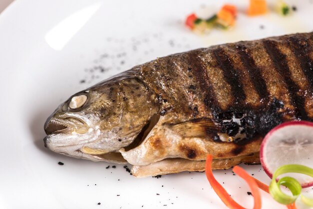 Carpa frita con limón, decorada con hierbas, aislada sobre fondo claro