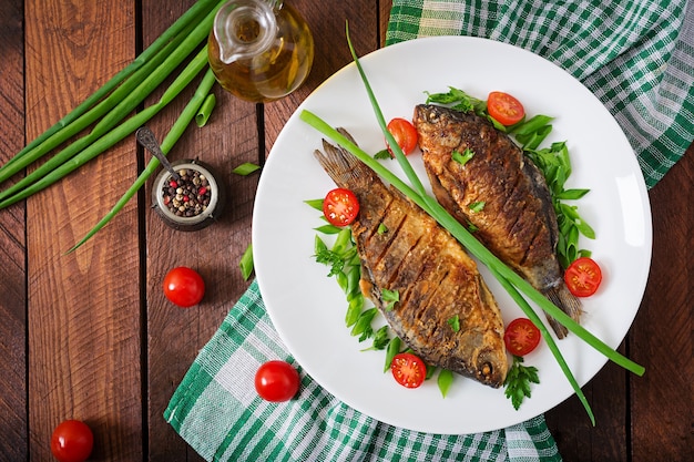 Carpa frita de los pescados y ensalada de las verduras frescas en fondo de madera.