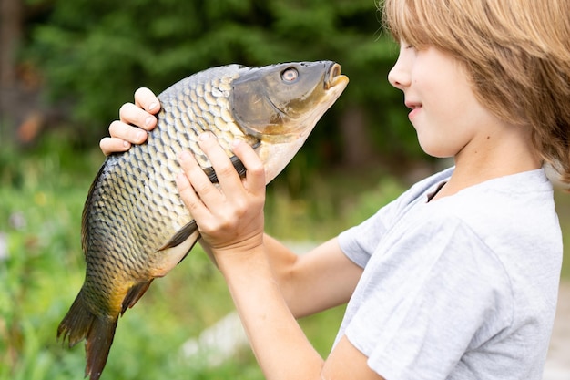 Foto carpa de pescado grande en manos de un niño pescando con un niño un joven pescador