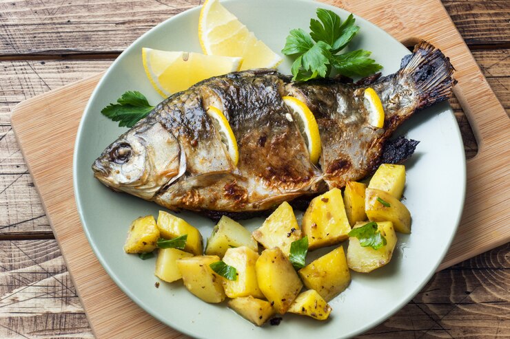 Carpa de pescados cocida al horno con verdes y patatas de limón en una placa. Fondo de madera