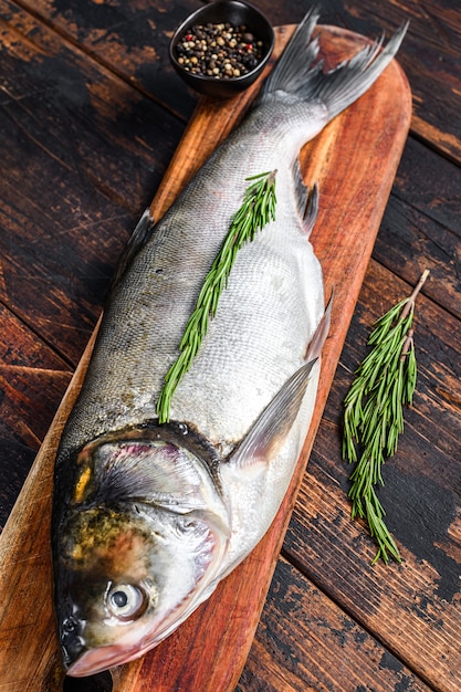 Carpa prateada de peixe inteiro cru em uma tábua com alecrim