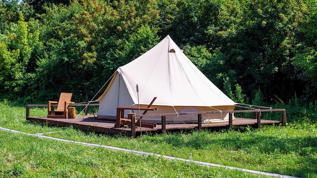 Carpa con sillas de madera frente a ella en glamping. Naturaleza, verdor alrededor