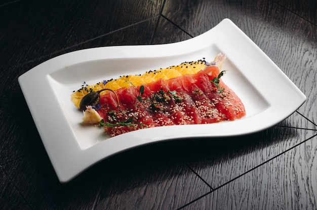 Carpaccio de atún con naranja sobre una placa blanca.