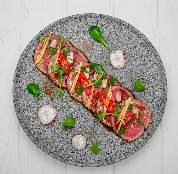 Carpaccio de carne com alho, molho de soja, pimenta malagueta e azeite em um prato escuro