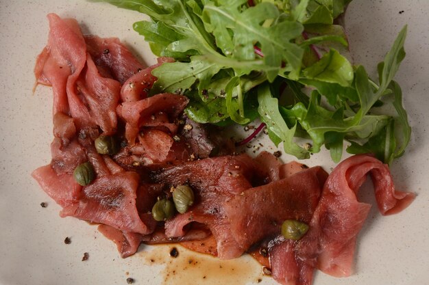 Foto carpaccio de carne com parmesão, alcaparras e rúcula. com azeite e molho de soja