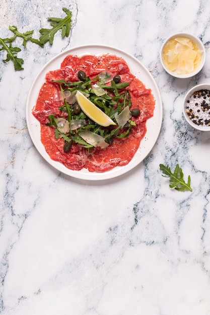 Carpaccio de carne marmoreada com rúcula, alcaparras, limão e queijo parmesão