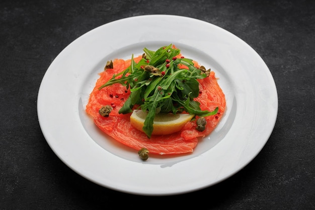 Carpaccio de salmão em um prato com limão em concreto