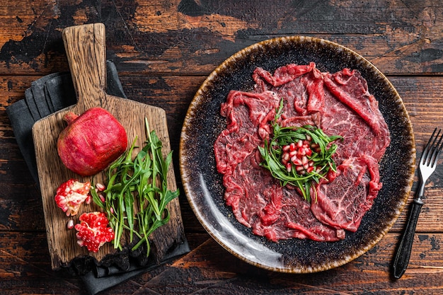 Carpaccio marmoreado carne bovina com rúcula e sementes de romã. fundo de madeira. vista do topo.