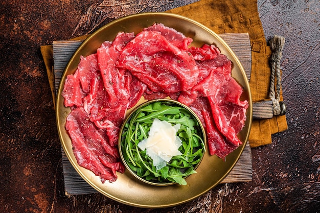 Carpaccio Rindfleisch-Vorspeise mit Parmesan und Rucola. Dunkler Hintergrund, Draufsicht